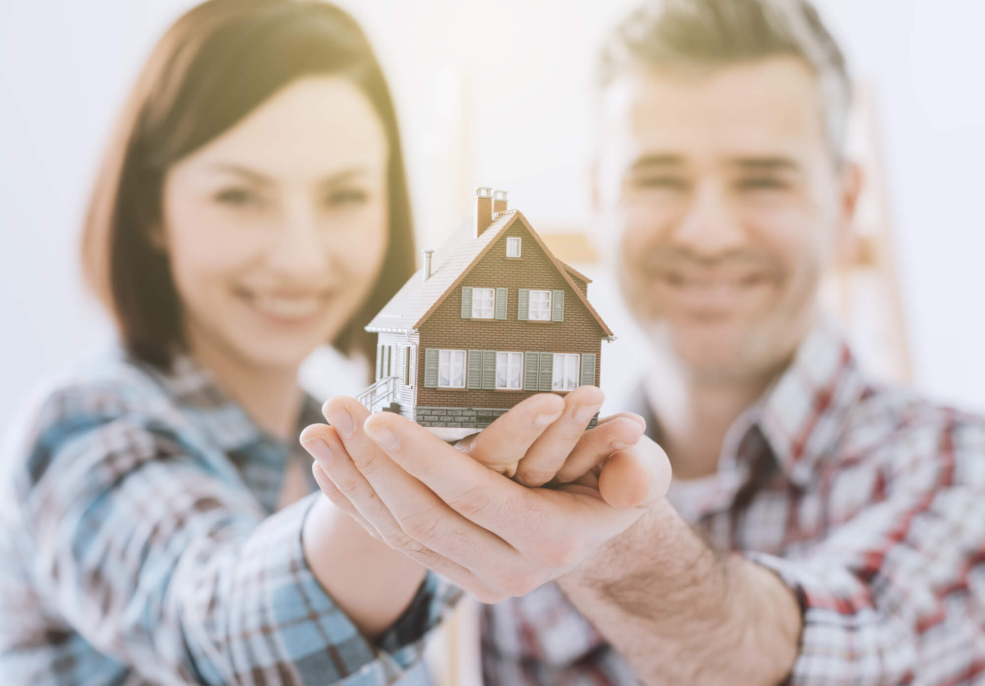 couple holding small model of house in outstretched hands